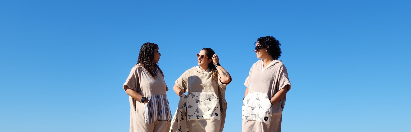 imagem três mulheres usando poncho e ao fundo um céu azul